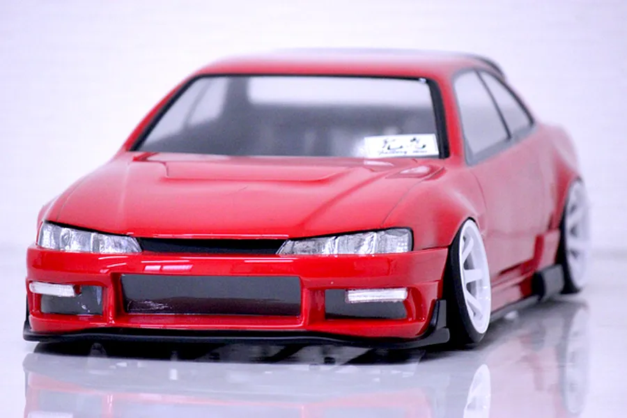 Red RC drift car body styled as a late model S14 Silvia with white wheels, parked on a reflective white surface.