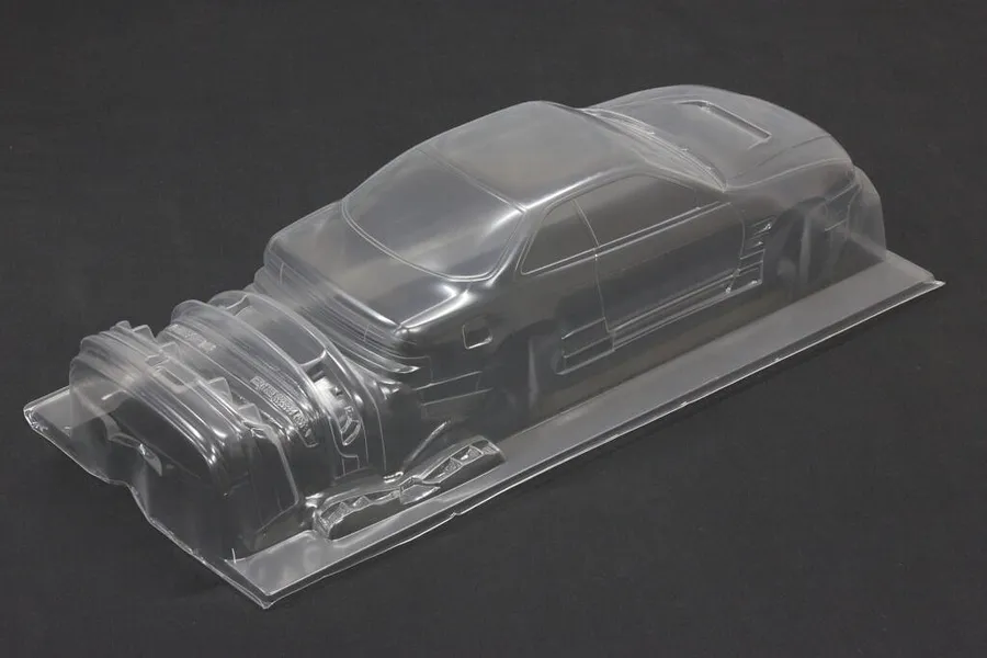 Unpainted clear polycarbonate RC drift car body shell with separate bumper and part moldings set against a dark background.