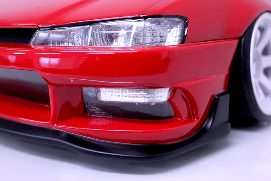 Close-up of the front bumper, headlight, and white wheel of a red RC drift car body shell.