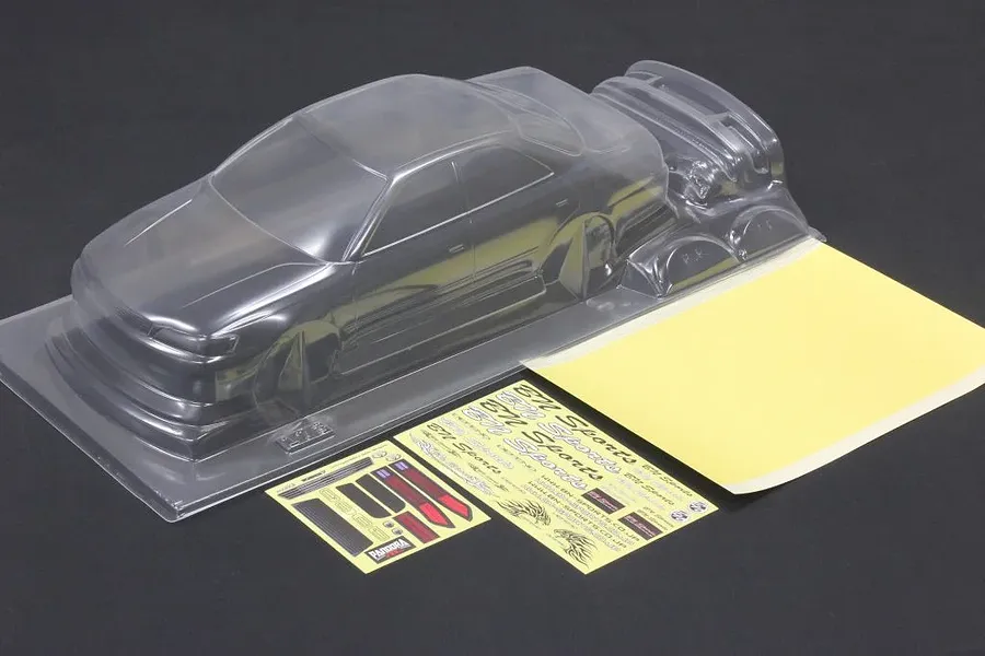 Unpainted clear polycarbonate RC car body shell with separate parts, decal sheets, and window masks on a dark surface.