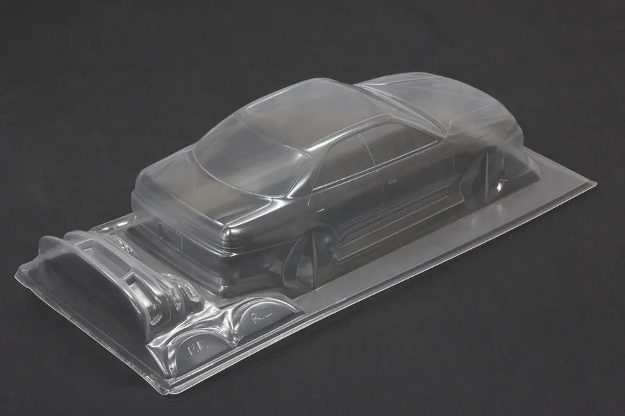 Unpainted clear polycarbonate RC drift car body shell with additional molded parts on a dark background.