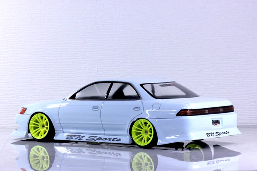 Side-rear view of a painted white RC drift car body shell with bright yellow wheels and BN Sports decals on a reflective surface.