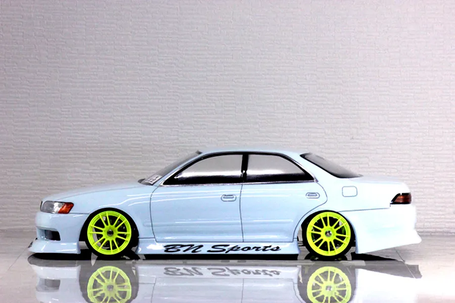 Side view of a light blue RC drift car body with bright yellow multi-spoke wheels and BN Sports branding on a reflective surface.