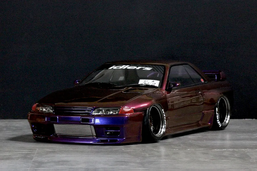 A Pandora RC BNR32 Skyline GT-R drift body shell in metallic purple, displayed on a studio floor with low-slung wheels and custom decals.