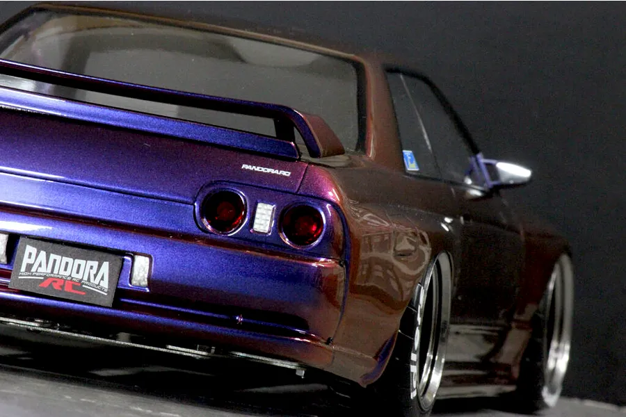Rear three-quarter view of a painted Pandora RC BNR32 Skyline GT-R body shell showing iridescent purple and bronze paint, rear spoiler, and custom license plate.