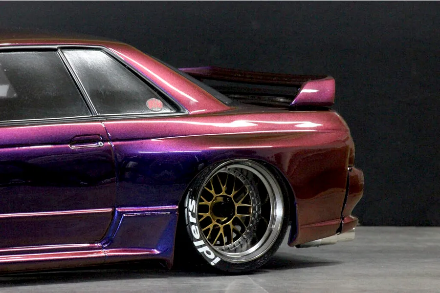 Close-up side profile of the rear section of a custom purple and pink shifting RC drift car body with gold mesh wheels.