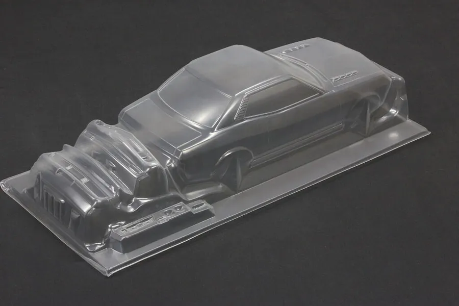 Unpainted clear polycarbonate RC car body shell with separate bumper and grille parts on a dark background.