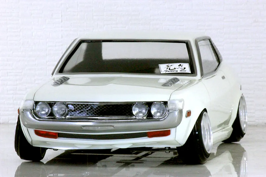 Front three-quarter view of a painted white RC drift car body shell mounted on a chassis with cambered wheels against a white brick wall background.