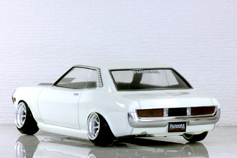 Rear-three-quarter view of a white RC drift car body on a reflective surface with white brick wall background.