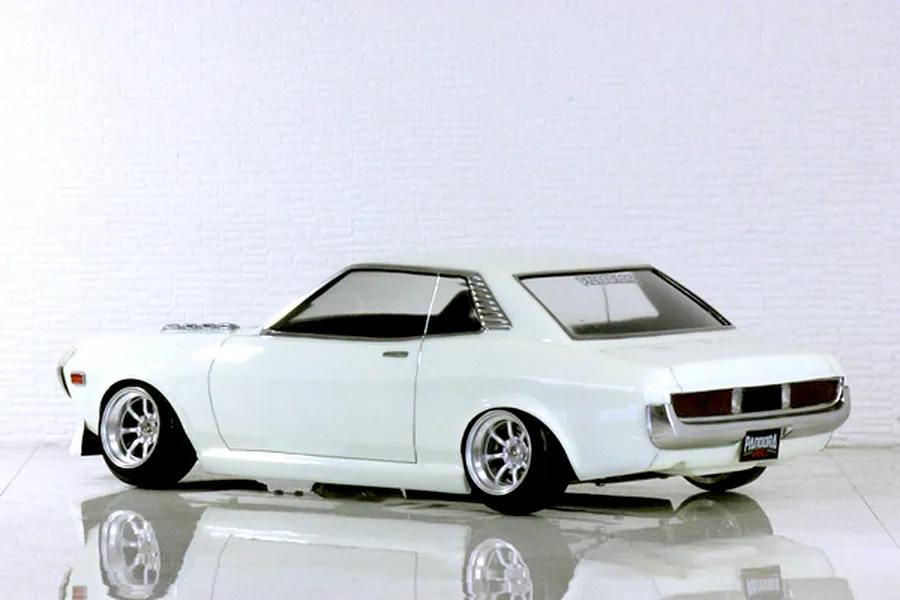 Rear three-quarter view of a white Toyota Celica RC drift car body shell with custom wheels and reflective floor.