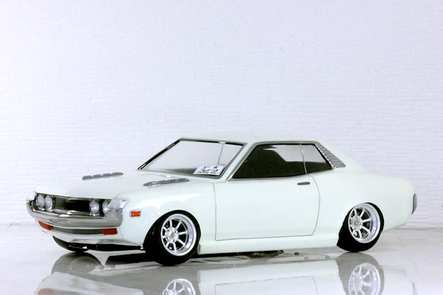 Side-profile view of a white Toyota Celica 1600GT RC body shell on a reflective white studio surface.