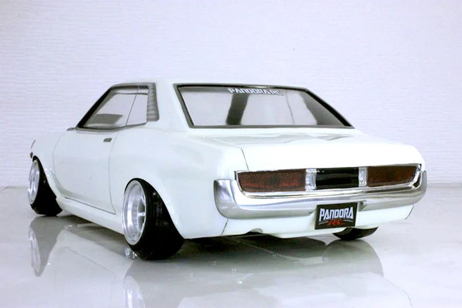 Rear three-quarter view of a painted white Toyota Celica 1600GT RC drift car body on a reflective white studio surface.