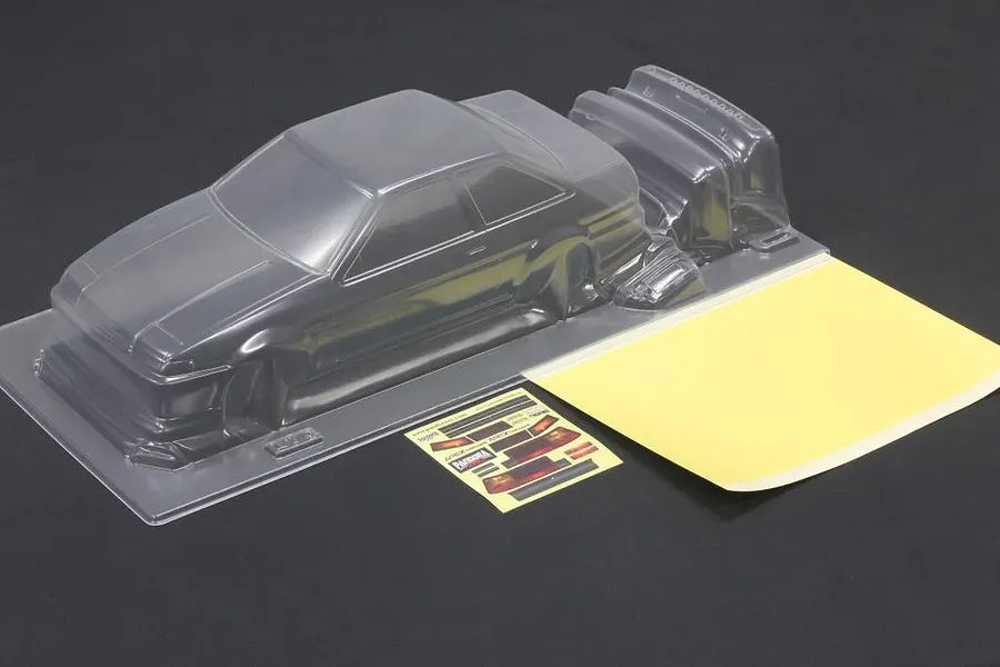 Unpainted clear polycarbonate RC car body shell with additional molded parts, window masks, and decal sheet on a dark surface.