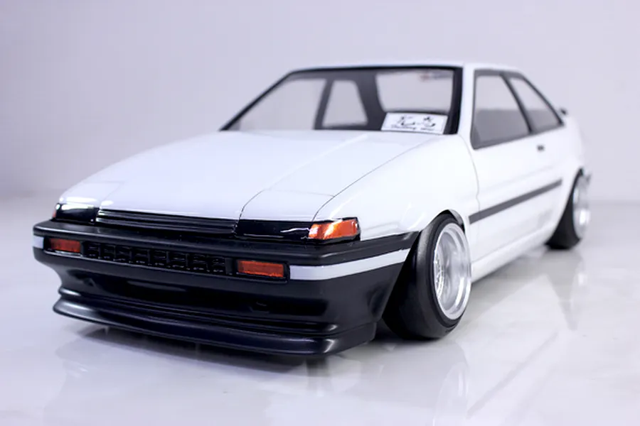 Front three-quarter view of a white RC drift car body shell modelled after a Toyota AE86 Trueno with black trim and custom wheels.