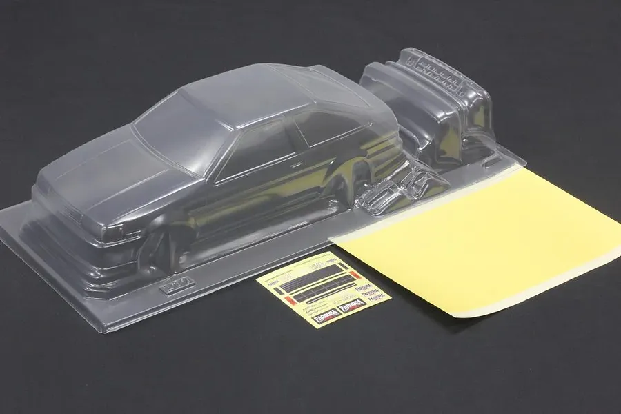 Unpainted clear polycarbonate RC car body shell with additional molded parts, window masks, and decal sheet on a dark surface.