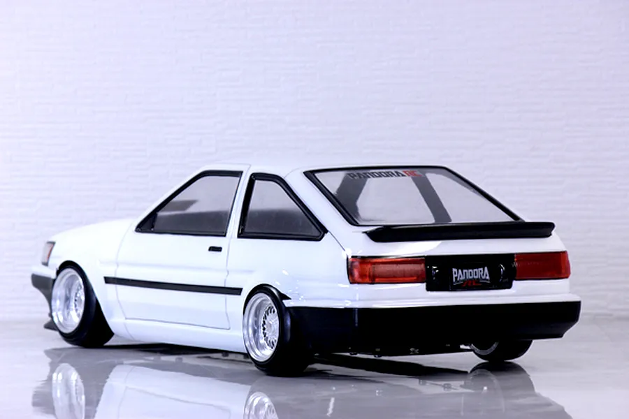 Rear-three-quarter view of a white RC drift car body styled like a Toyota AE86 Corolla Levin on a reflective white surface.