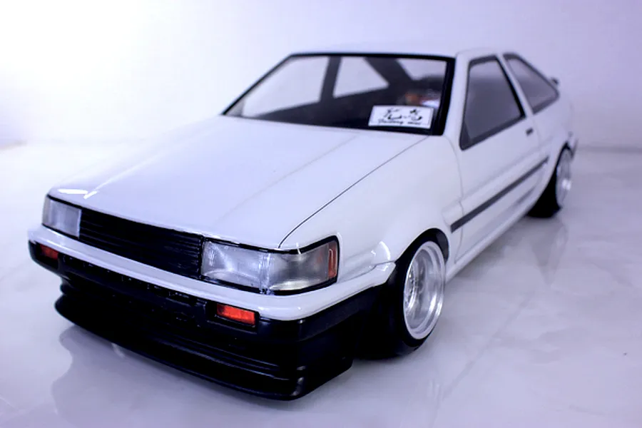 Front three-quarter view of a painted white Toyota AE86 Corolla Levin RC drift car body shell mounted on a chassis.