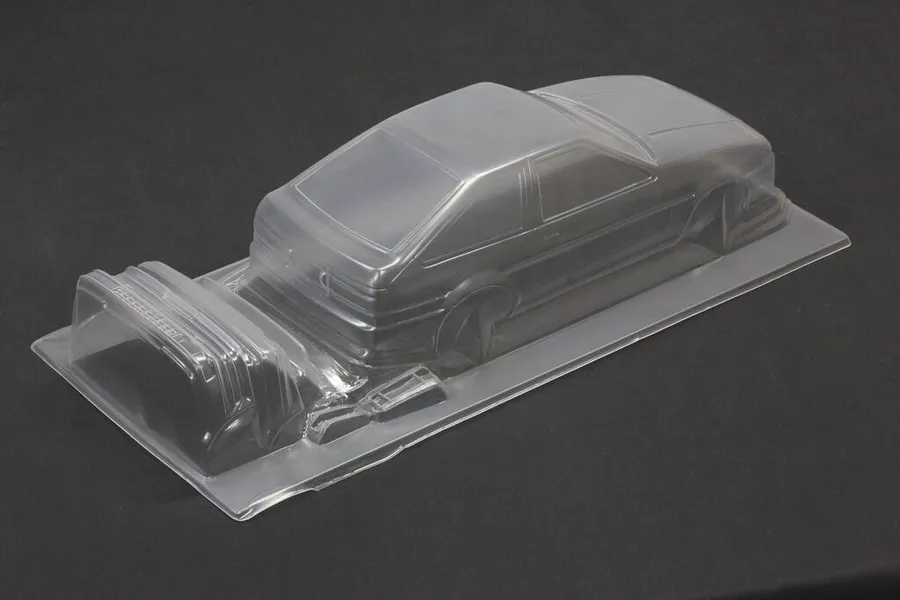 Unpainted clear polycarbonate RC car body shell of a Toyota AE86 Sprinter Trueno 3-door on a dark surface.