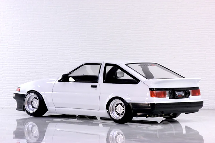 Rear-three-quarter profile view of a white Toyota AE86 Sprinter Trueno RC drift car body on a reflective white studio surface.