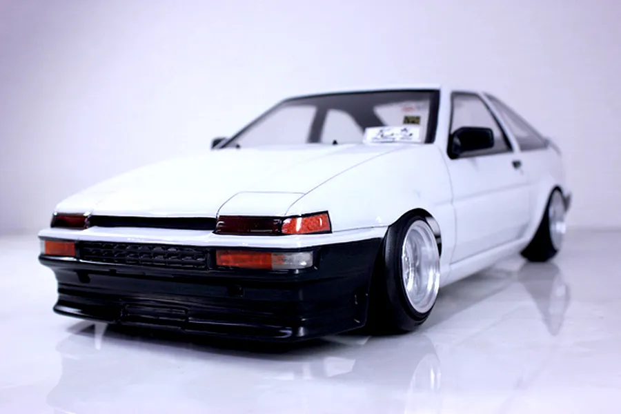 Low angle front-three-quarter view of a white RC drift car body styled after a Toyota AE86 Trueno with custom deep dish wheels.
