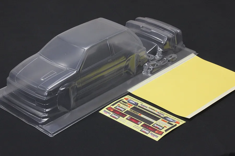 Unpainted clear polycarbonate RC car body shell with additional molded parts, decal sheet, and masking sheet on dark background.