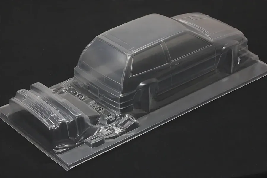 Unpainted clear polycarbonate RC body shell of a Honda Civic Si with separate bumper and accessory parts on a dark background.