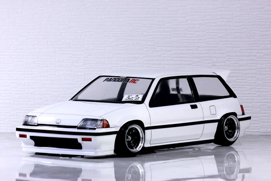 White Honda Civic Si RC drift body shell mounted on an RC chassis against a white brick wall background.