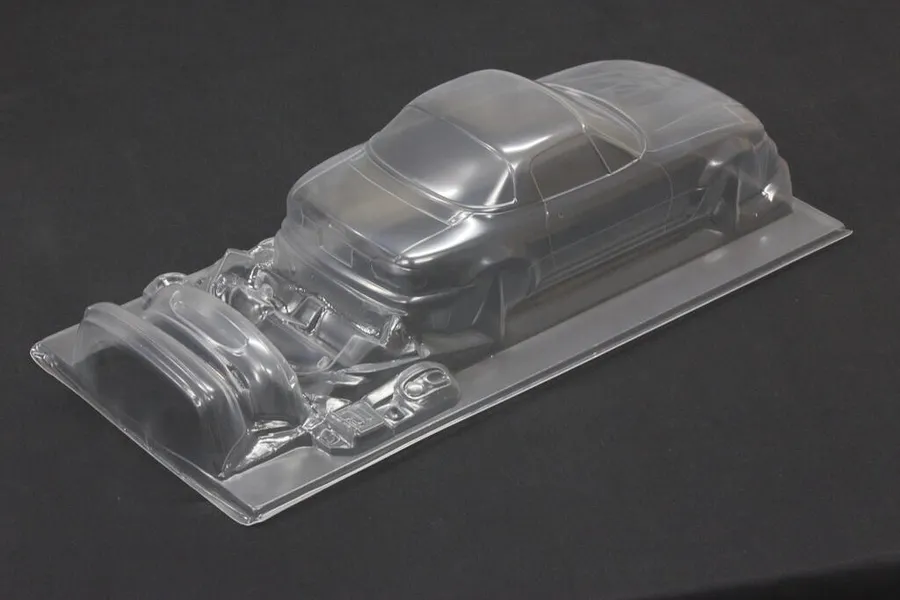 Unpainted clear polycarbonate RC car body shell for a Mazda Eunos Roadster showing main body and molded accessories.