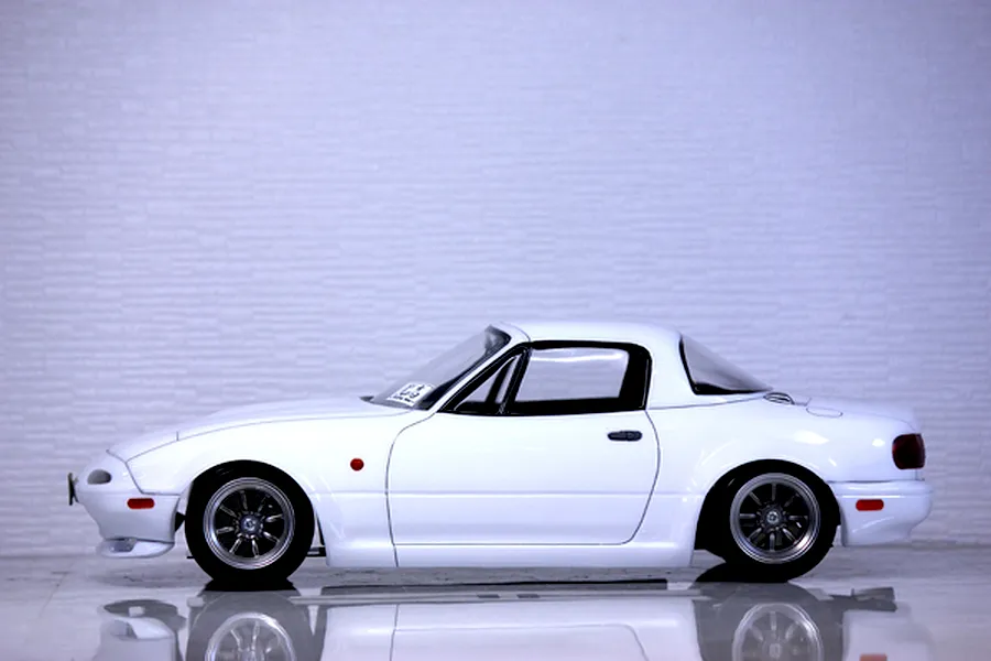 Side profile view of a painted white Mazda Eunos Roadster NA RC body shell mounted on a chassis with multi-spoke wheels.