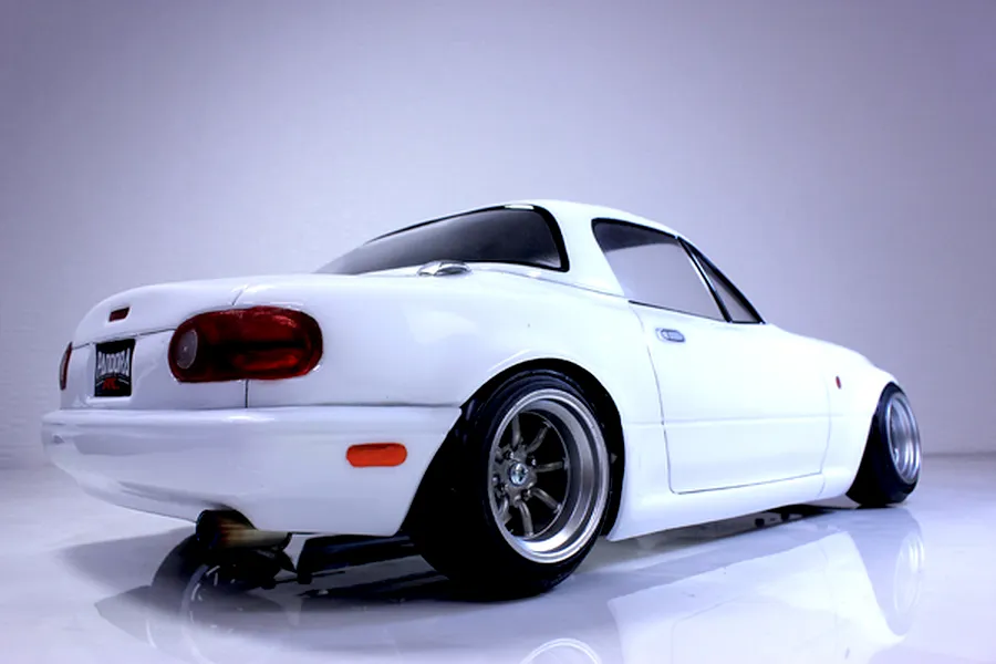 Rear-quarter view of a white RC drift car body styled like a Mazda Eunos Roadster with custom wheels and exhaust.