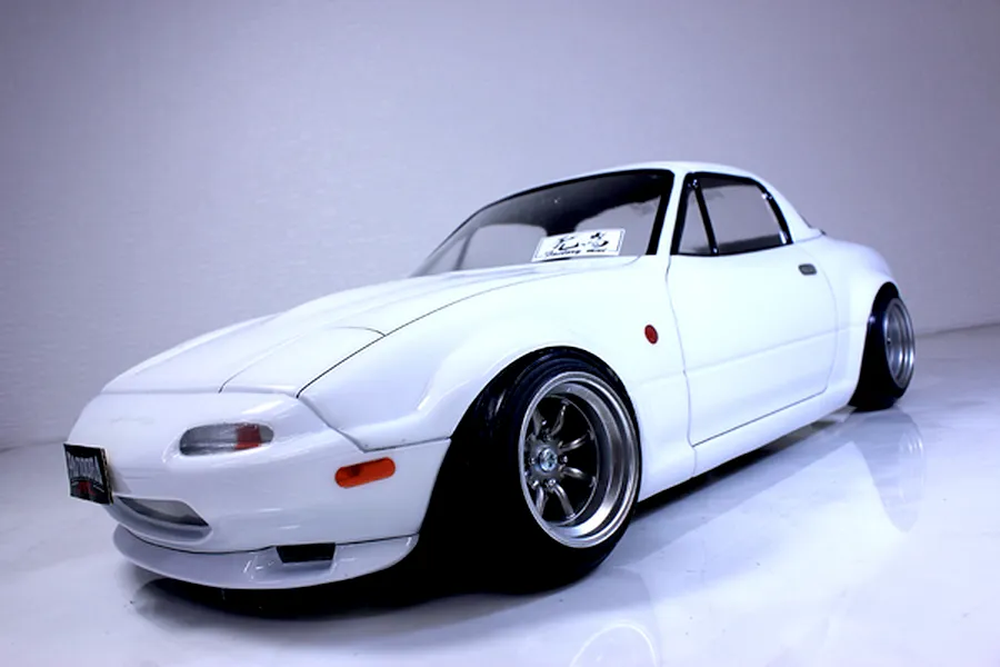 Low angle studio shot of a white Pandora RC Mazda Eunos Roadster NA drift body shell mounted on an RC chassis with deep dish wheels.