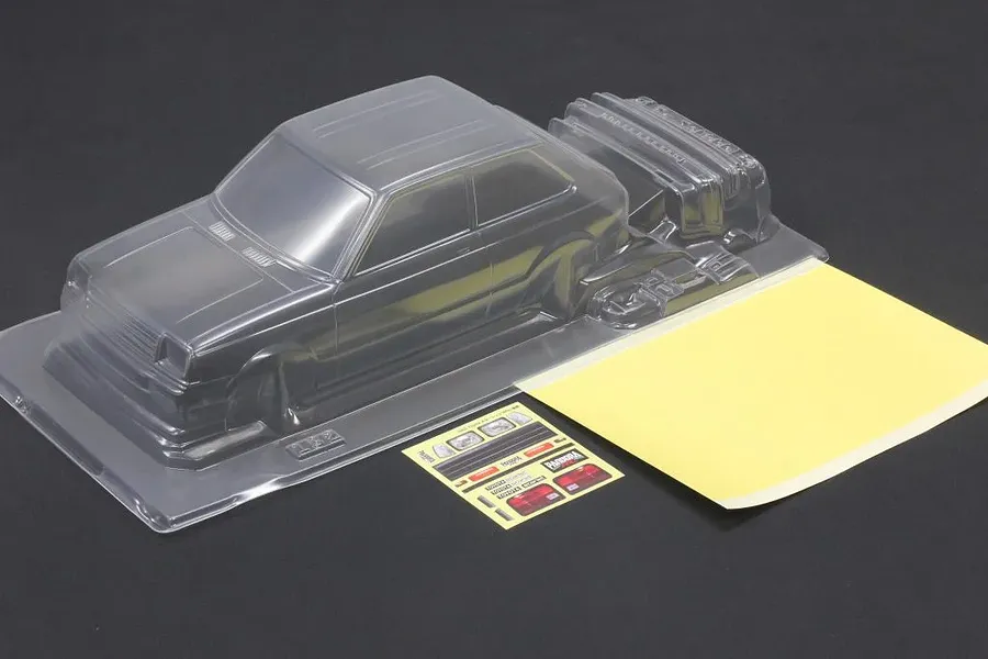 Unpainted clear polycarbonate RC body shell of a Toyota Starlet KP61 with included decals and masking sheet on a dark background.