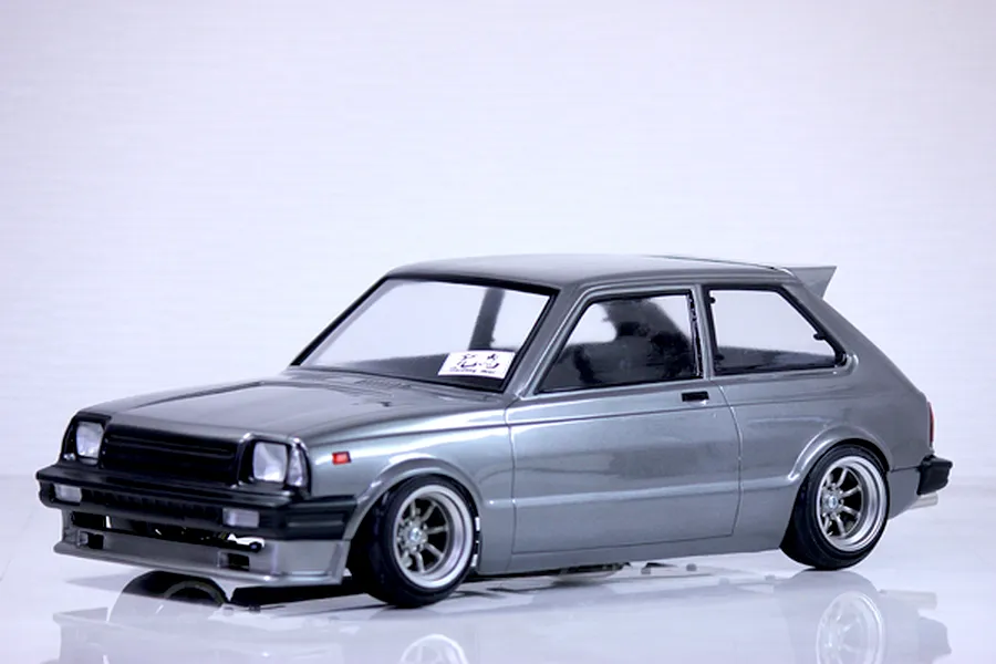A painted grey Toyota Starlet KP61 RC drift car body shell mounted on a chassis with custom wheels against a white background.