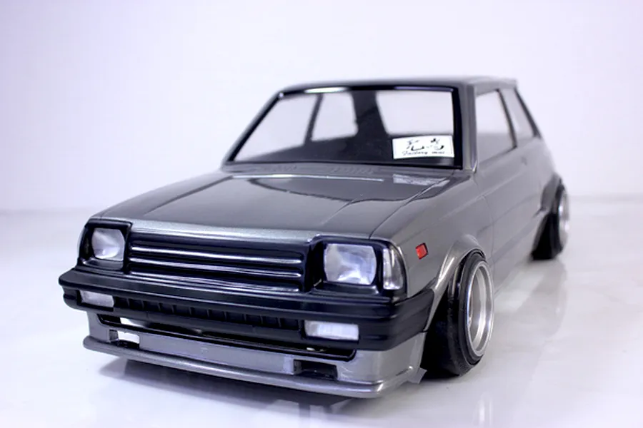 Painted grey RC drift car body shell mounted on a chassis with wheels against a white studio background.