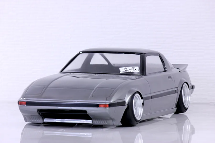 Grey Mazda Savanna RX-7 SA22C drift RC car body shell with aftermarket deep dish wheels in a studio setting.