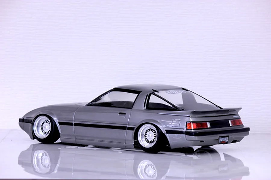 Rear-three-quarter studio view of a silver Mazda Savanna RX-7 SA22C RC drift car body shell on a reflective white surface.