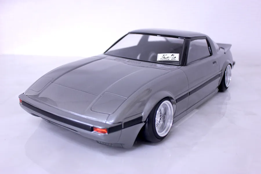 A painted silver RC body shell of a Mazda Savanna RX-7 SA22C displayed on a white surface.
