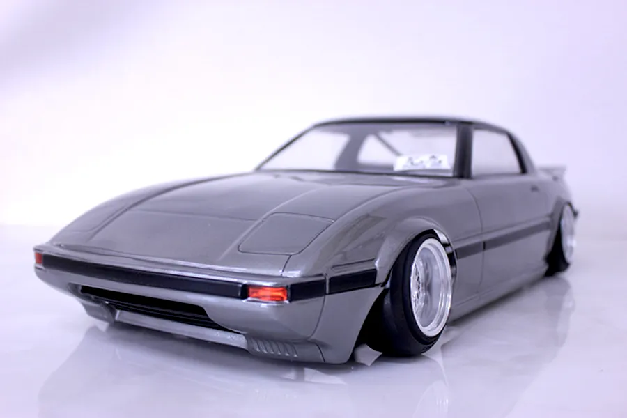 Painted grey Mazda Savanna RX-7 RC drift car body shell mounted on a chassis with custom wheels against a white background.