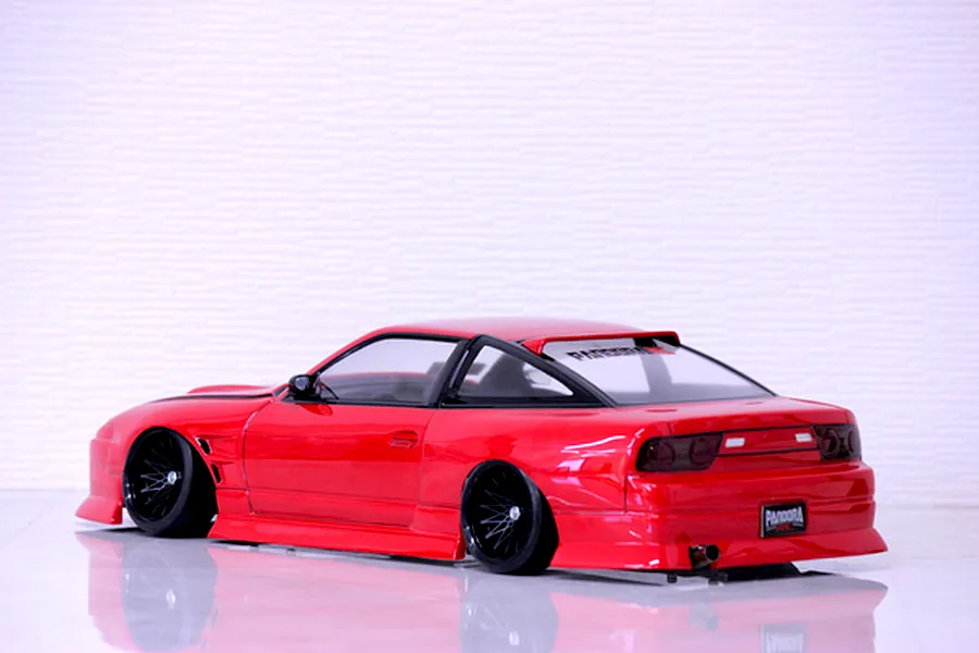 Rear quarter view of a red Pandora RC RPS13 180SX drift car body shell with black multi-spoke wheels on a glossy white surface.