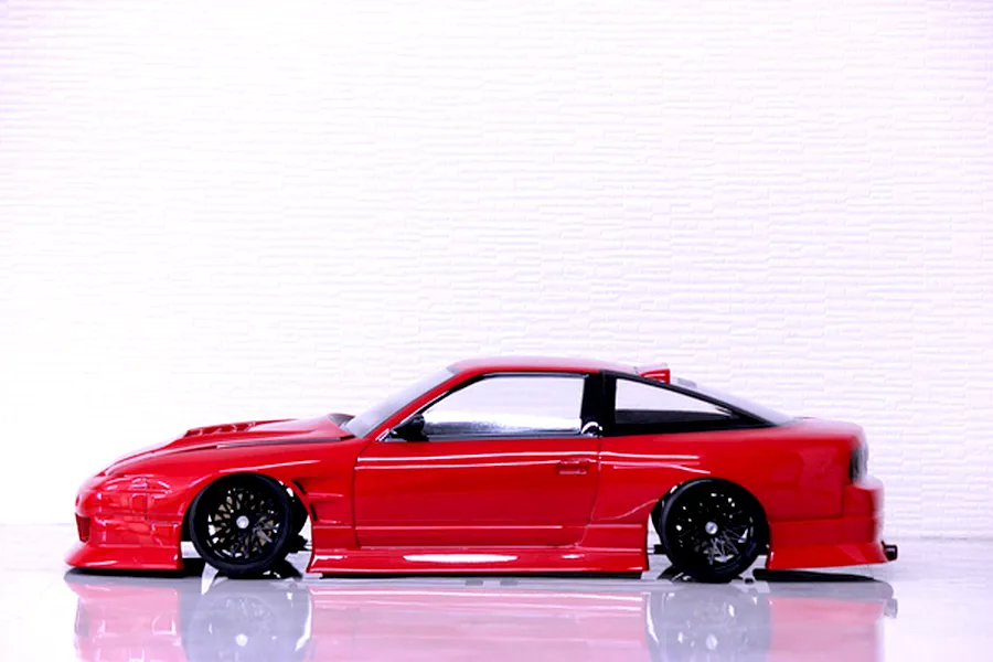Side profile view of a red RC drift car body shell mounted on a chassis with black wheels against a white background.