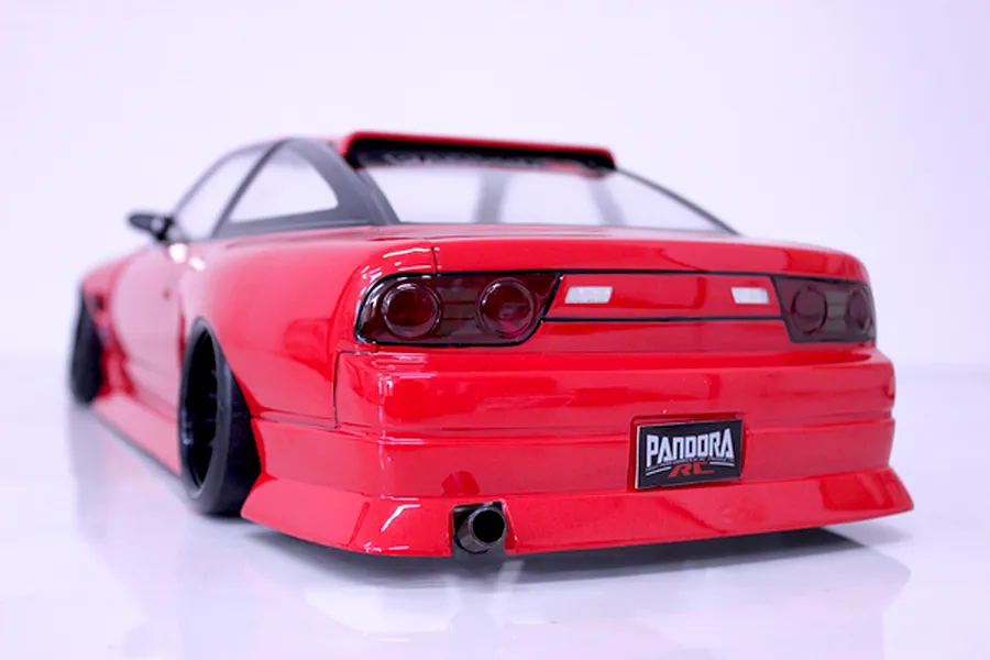 Rear three-quarter view of a painted red Pandora RC drift car body with black wheels and exhaust tip on a white surface.