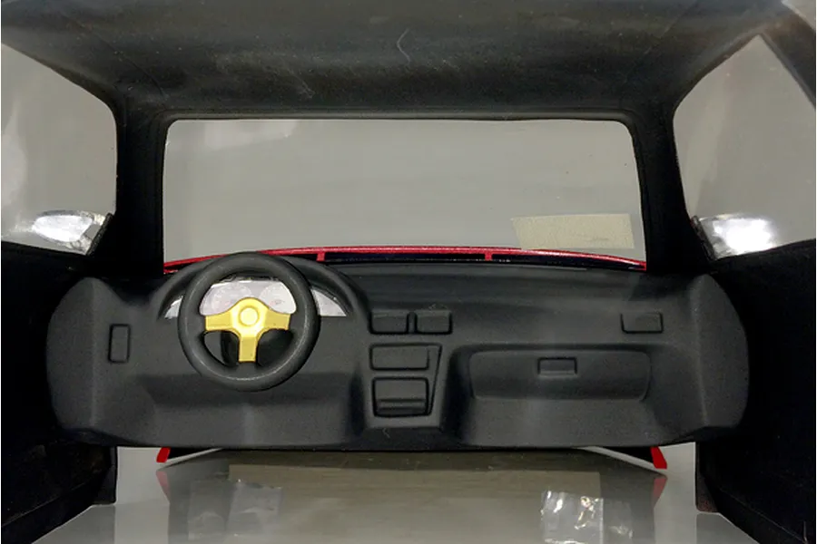 Interior view of an RC car body shell featuring a black dashboard and steering wheel with a gold center.