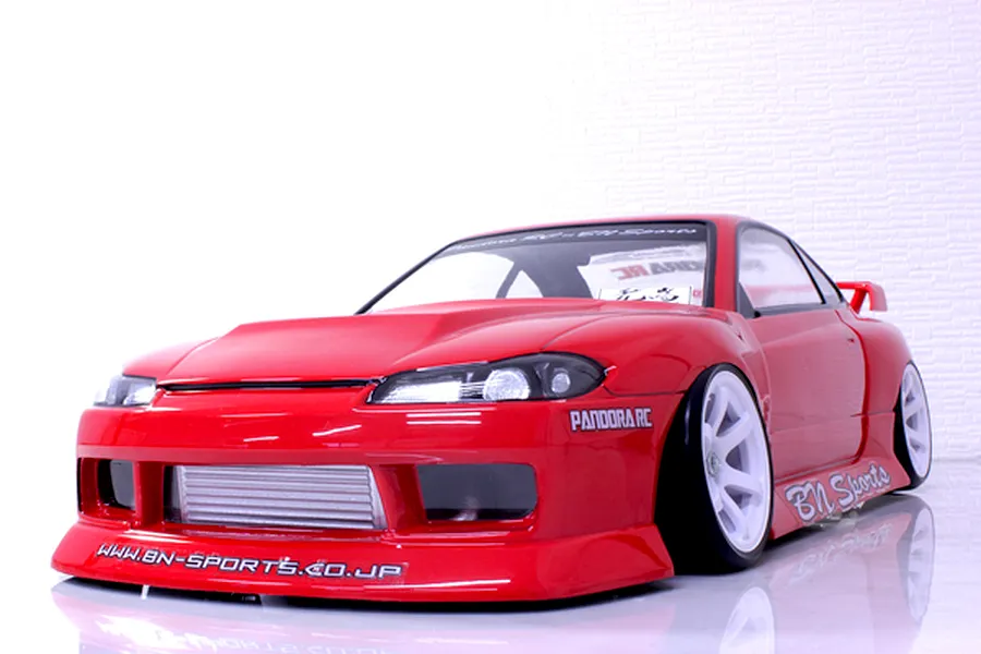 A painted red RC drift car body shell mounted on a chassis with white wheels against a white background.