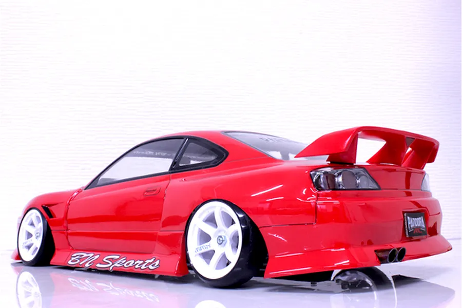Rear three-quarter view of a red RC drift car body shell, featuring a large rear wing, white wheels, and BN Sports decals.