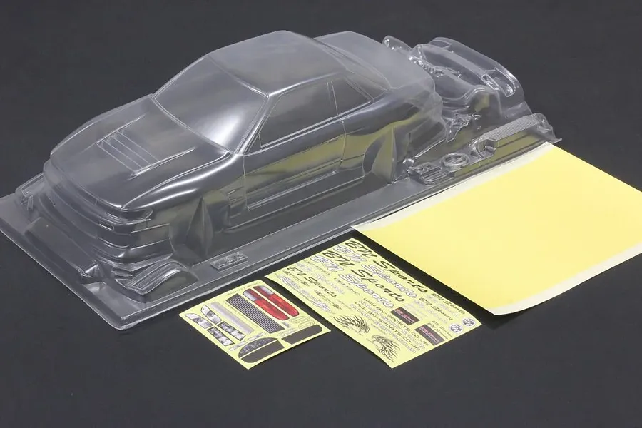 Unpainted clear RC car body shell with separate decal sheets and masking film on a dark surface.