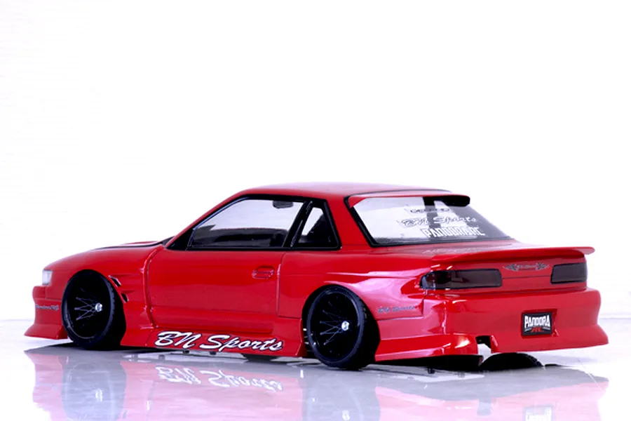 Rear-three-quarter profile of a red Pandora RC S13 Silvia drift car body featuring BN Sports decals and black multi-spoke wheels on a reflective white surface.
