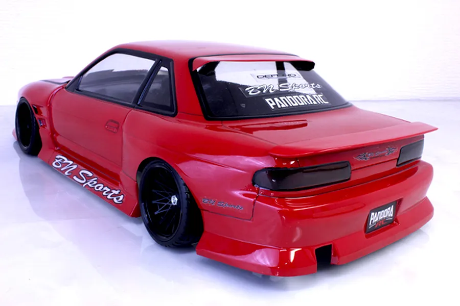 Rear-three-quarter view of a painted red Nissan S13 Silvia RC drift car body shell featuring BN Sports decals and black multi-spoke wheels.