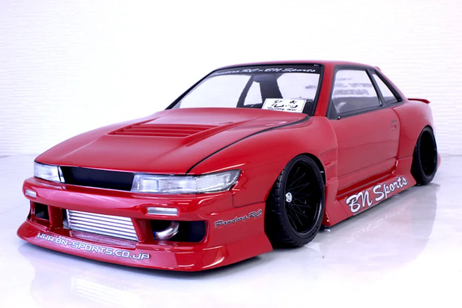 Red Pandora RC S13 Silvia drift car body shell with BN Sports decals, front mount intercooler, and black multi-spoke wheels on a reflective surface.