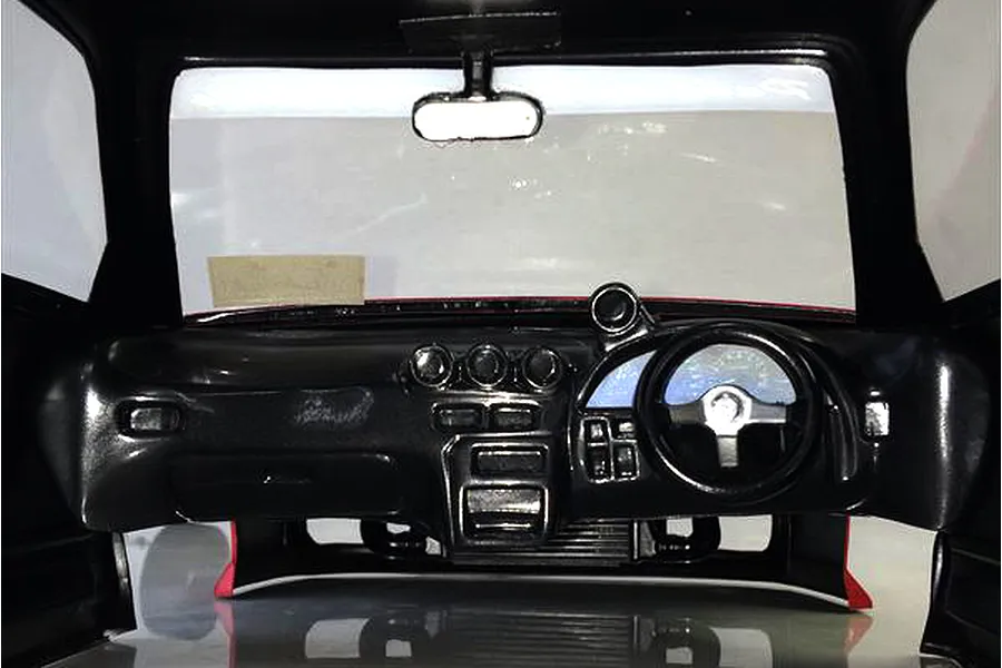 Interior view of an RC car body shell showing a detailed black dashboard, steering wheel, and rearview mirror.