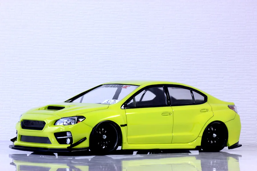 A studio view of a bright yellow Subaru WRX STI RC drift car body shell mounted on a chassis with black wheels.